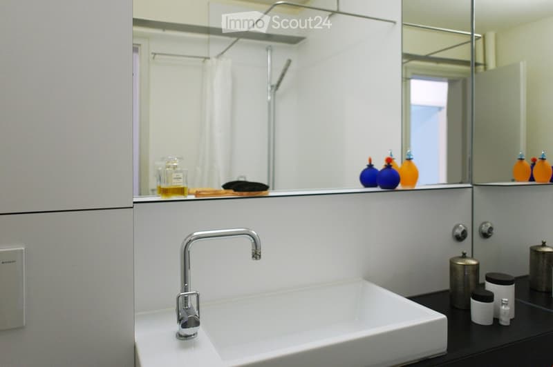 Modern bathroom with a white sink, chrome faucet, large mirror, and various cosmetic items on the counter.