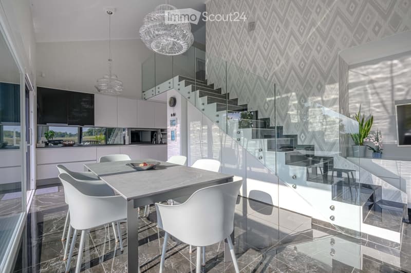 Furnished Room. Modern dining area with a glass table, white chairs, and a glass staircase. The room has a marble floor and a patterned wall.