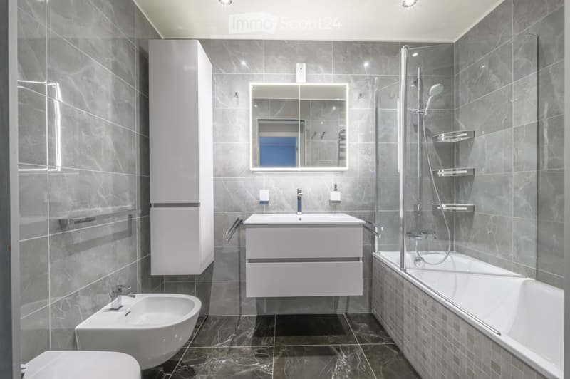 Bathroom. Modern bathroom with gray tiles, white fixtures, and a bathtub with a glass shower enclosure.