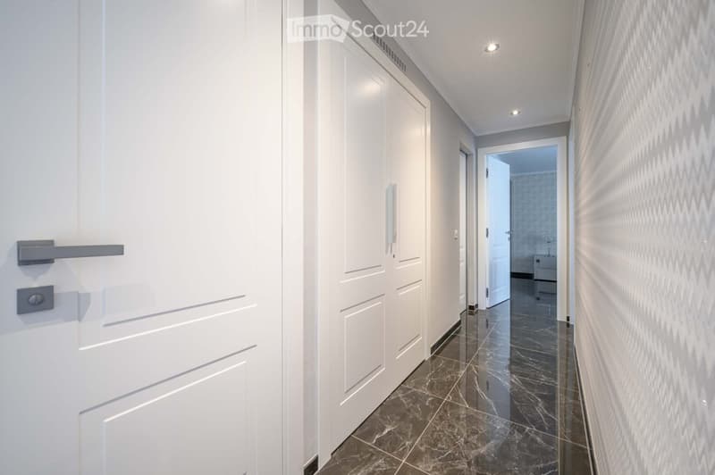 Corridor / Hallway. Empty corridor with white doors, marble flooring, and a chevron pattern on the wall.