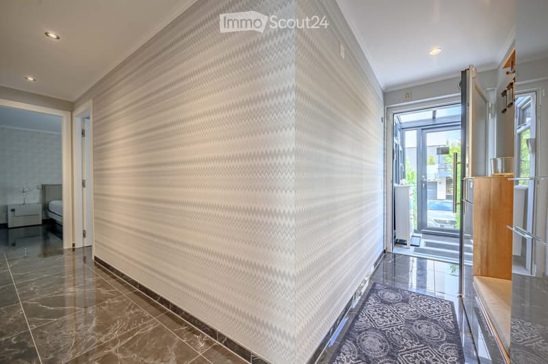 Corridor / Hallway. A hallway with a zigzag patterned wall, marble flooring, and a rug. There is a bed and nightstand in the background.