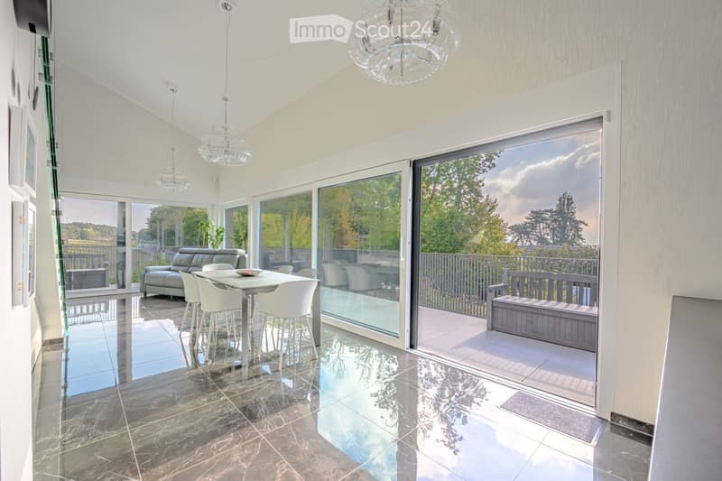 Furnished Room. Modern dining area with a table, chairs, and a couch. Large glass doors leading to a balcony with a bench. Chandeliers and a plant add to the decor.