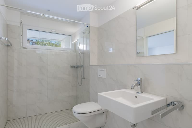 Modern bathroom with white marble tiles, a toilet, a sink with a modern faucet, a large mirror, and a glass-enclosed shower with a window.