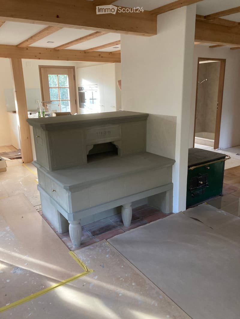 A partially furnished room with a stove, cabinet, sink, and faucet, featuring exposed wooden beams and a tiled floor.