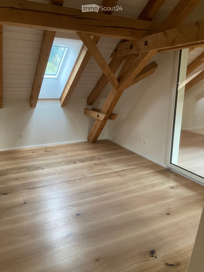 Empty room with wooden flooring and exposed wooden beams, featuring a skylight window and a sliding glass door.