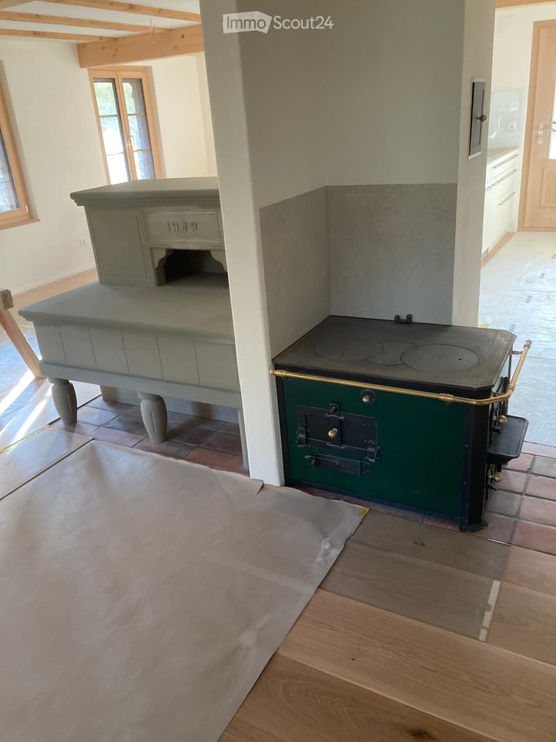 A rustic kitchen with a green stove and a stone countertop, featuring wooden flooring and large windows.