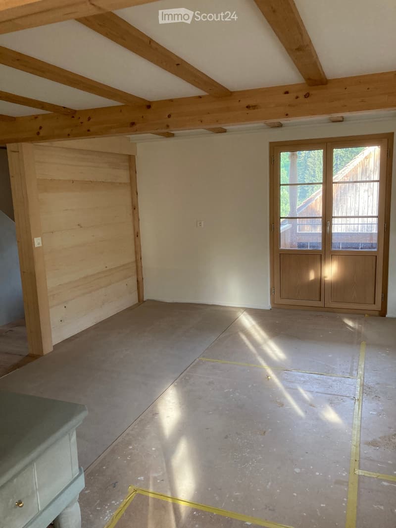 Empty room with exposed wooden beams, tiled floor, and large sliding glass door leading outside.