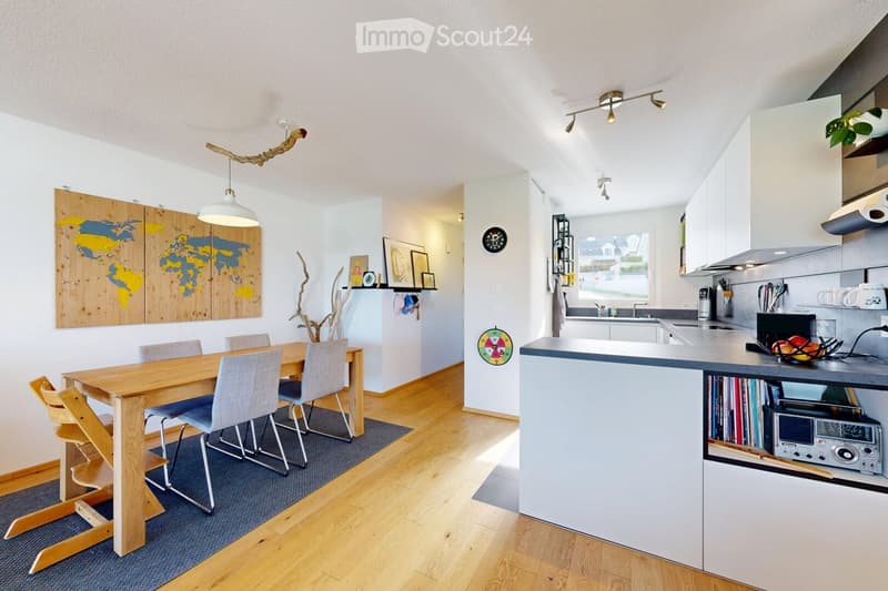 Open-plan kitchen and dining area with modern white cabinets, wooden dining table, four chairs, and a kitchen island with a sink and various appliances.