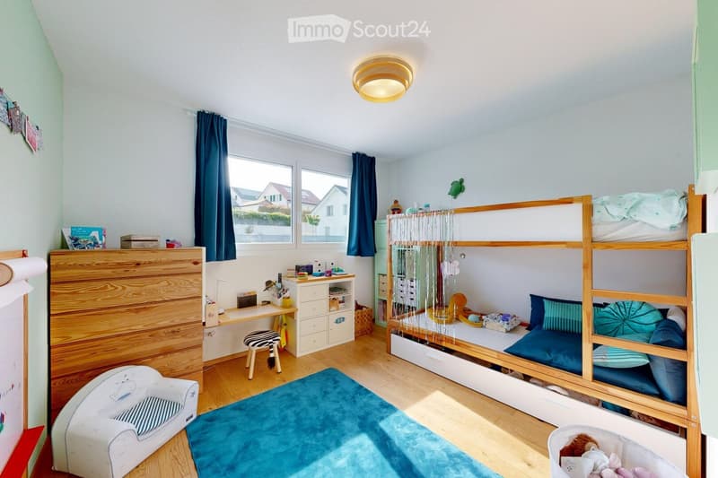 A cozy children's bedroom with a bunk bed, a small chair, a desk, a cabinet, and a rug.