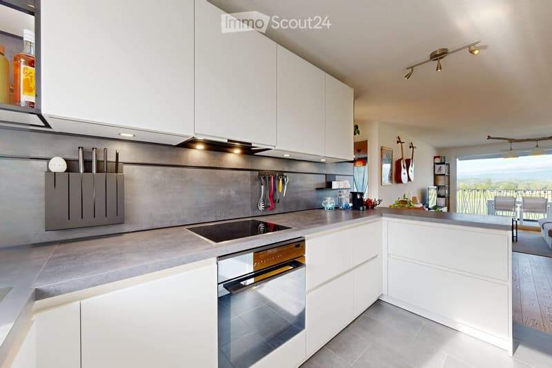 Modern kitchen with white cabinets, a central island, induction cooktop, and built-in dishwasher. Features include a knife block, various kitchen utensils, and a view to an outdoor area with a table and chairs.
