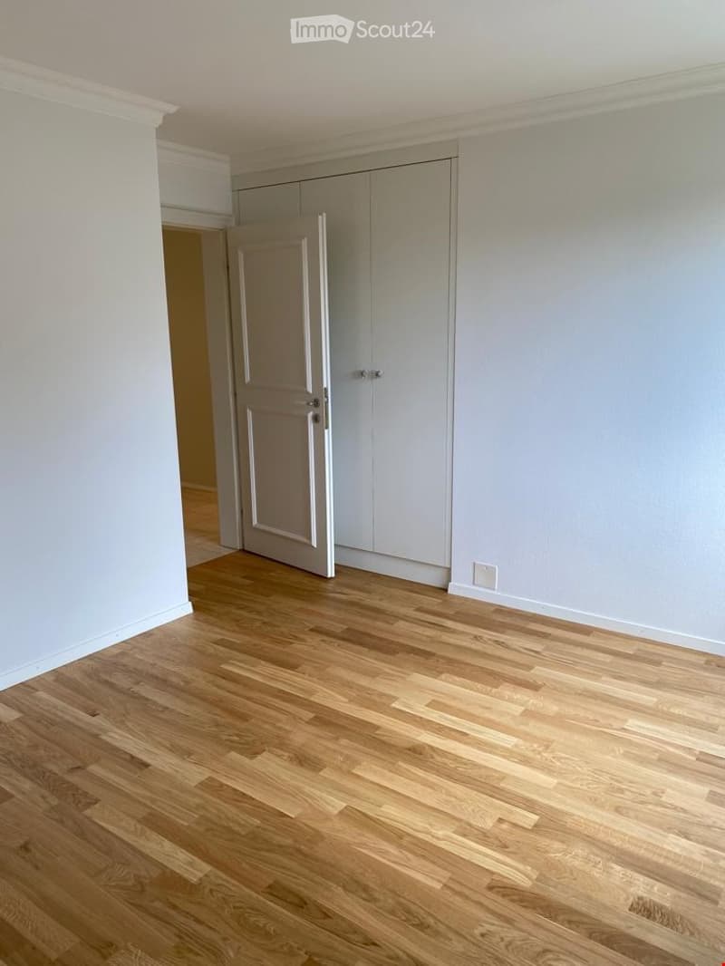 Empty room with light grey walls, wooden flooring, and built-in wardrobes.