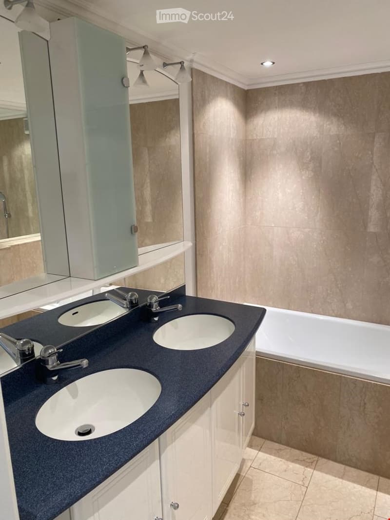 Modern bathroom with three sinks, a large mirror, and a bathtub, featuring sleek dark countertops and white cabinetry.