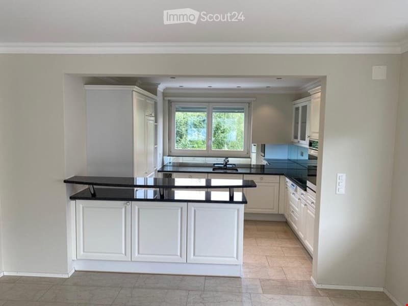 Modern kitchen with white cabinets, black countertops, and a large window overlooking greenery.