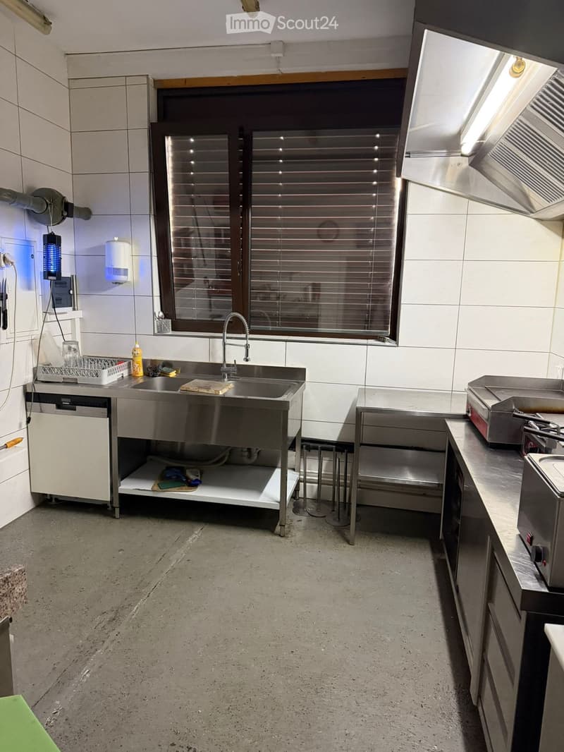 Stainless steel countertops, sink with faucet, oven, cabinets, tiled walls, window with blinds, small dishwasher, light above oven, and a countertop oven.