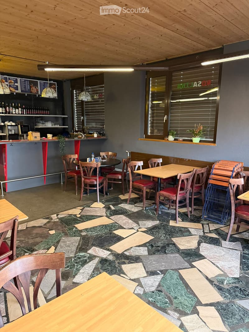 Wooden ceiling, mosaic tile floor, wooden tables and chairs, countertops with various drinks, window with blinds, plants, menu boards on wall