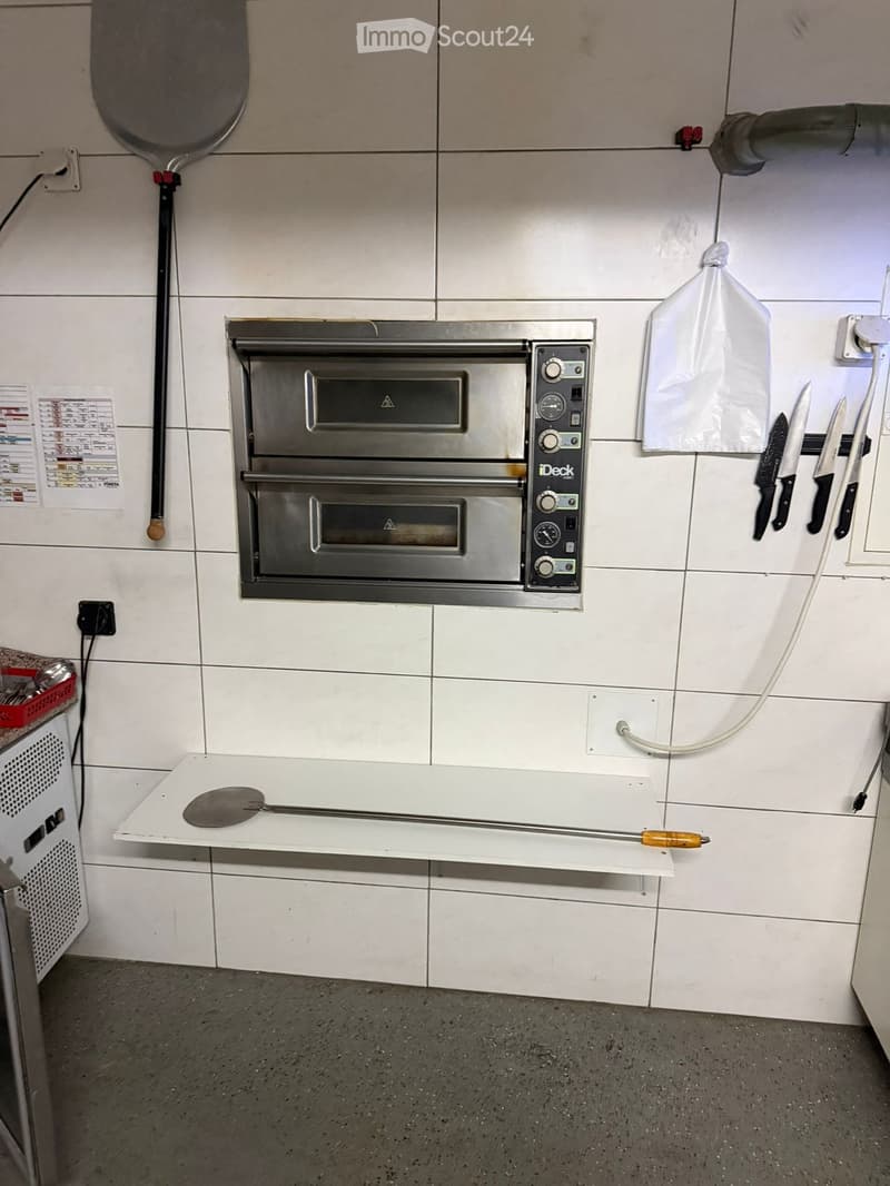 Commercial kitchen: oven, pizza spatula, knives, white tiled wall, stainless steel shelves, power outlet