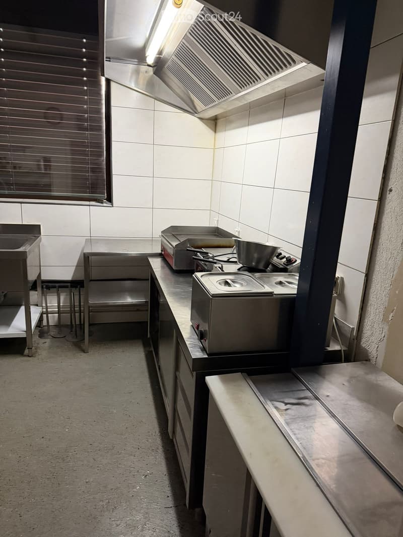 commercial kitchen, stainless steel countertops, industrial appliances, overhead ventilation, white tile walls, cabinets, and open space.
