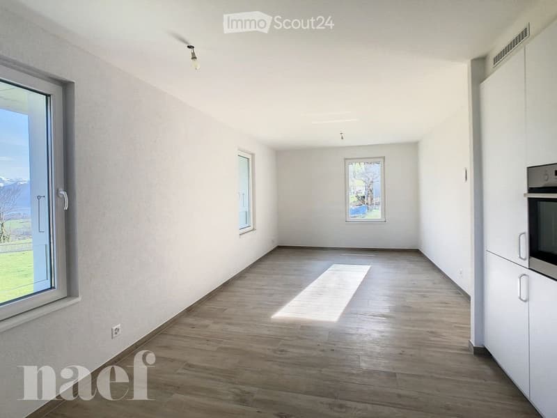 Empty room with wooden flooring, white walls, and large windows allowing natural light. No furniture or equipment present.