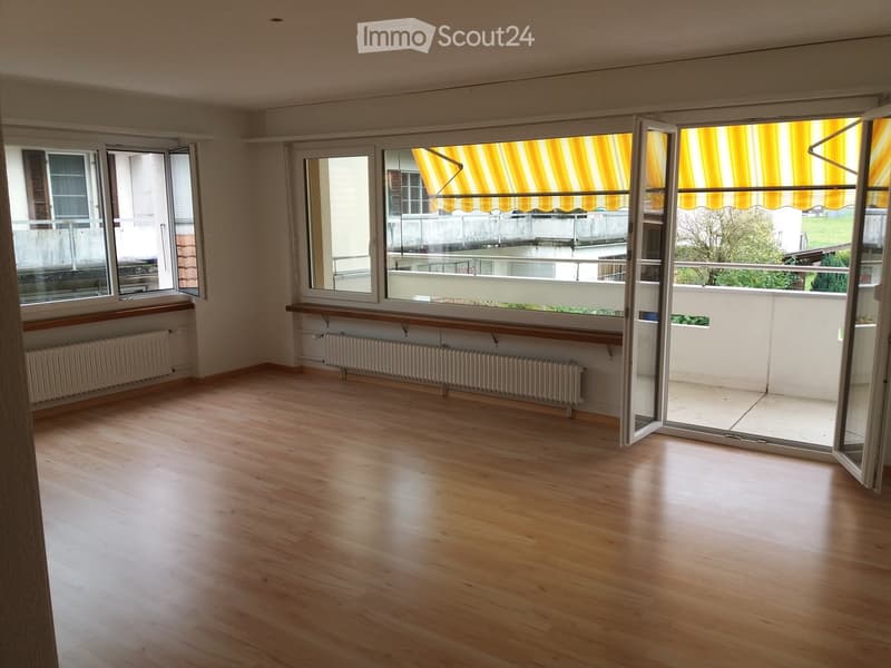 Empty room with wooden flooring, large windows, radiators, and sliding glass doors leading to a balcony.