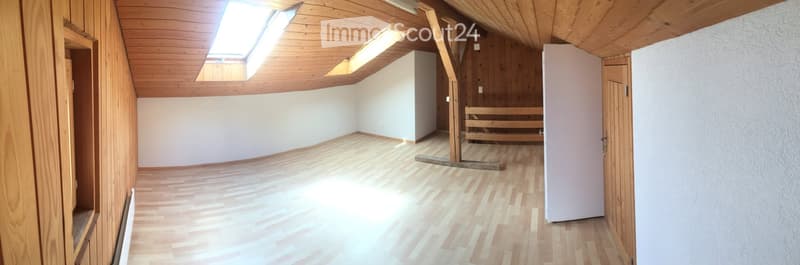 Empty attic room with wooden walls, ceiling, and floor, featuring skylights and a closed door.