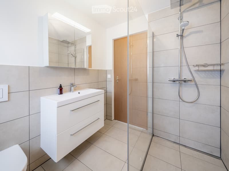 Modern bathroom with a white sink cabinet, mirror, glass-enclosed shower, and a bottle on the sink.