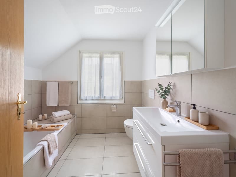 Modern bathroom with a bathtub, sink, mirror, and neatly arranged towels. Features a large window with sheer curtains and a small plant on the sink counter.