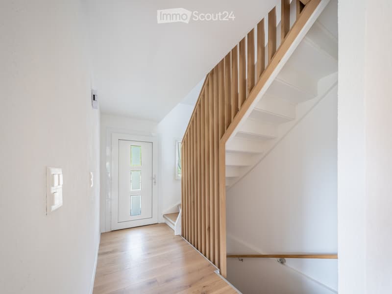 Modern hallway with wooden staircase, white walls, and a white door with glass panels.