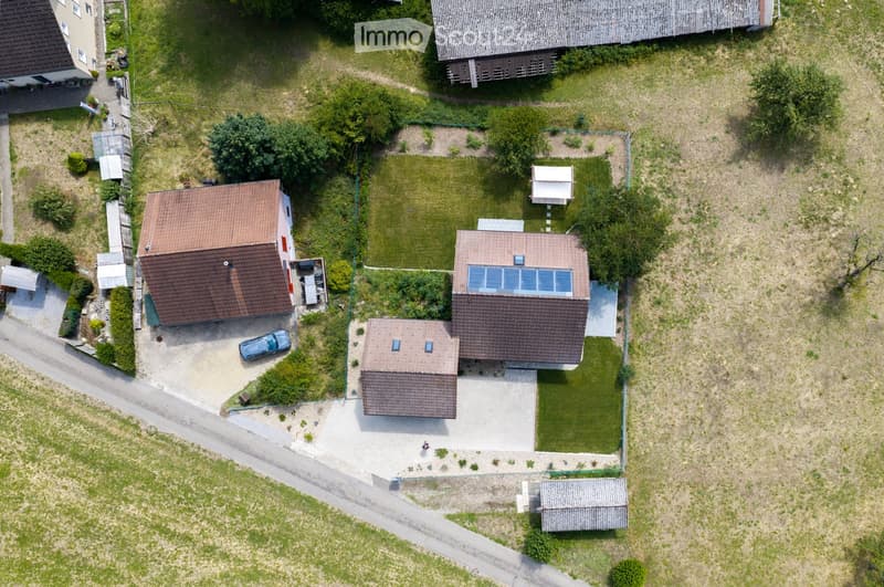 Aerial view of a residential property with multiple buildings, including a main house, a garage, and outbuildings, surrounded by a well-maintained lawn and garden area.