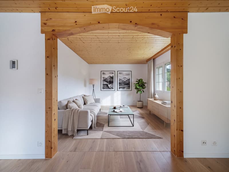 Modern living room with light wooden floors, white walls, a grey sofa, coffee table, floor lamp, sideboard, plant, and artwork.