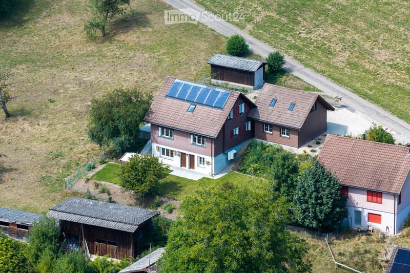 Aerial view of a residential area with multiple houses, solar panels, and surrounding greenery.