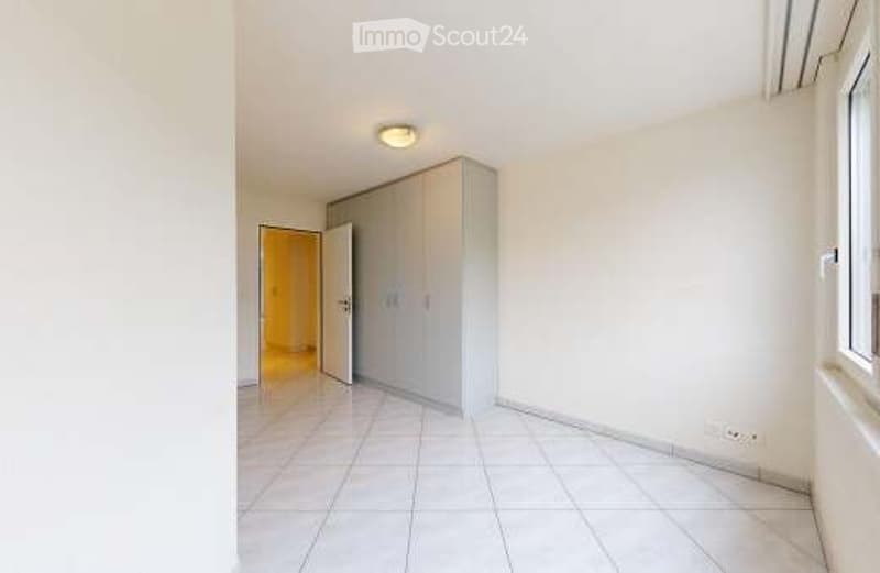 Empty room with white tiled flooring, white walls, a built-in wardrobe, and a ceiling light fixture. The room is unfurnished and appears to be a bedroom or storage space.