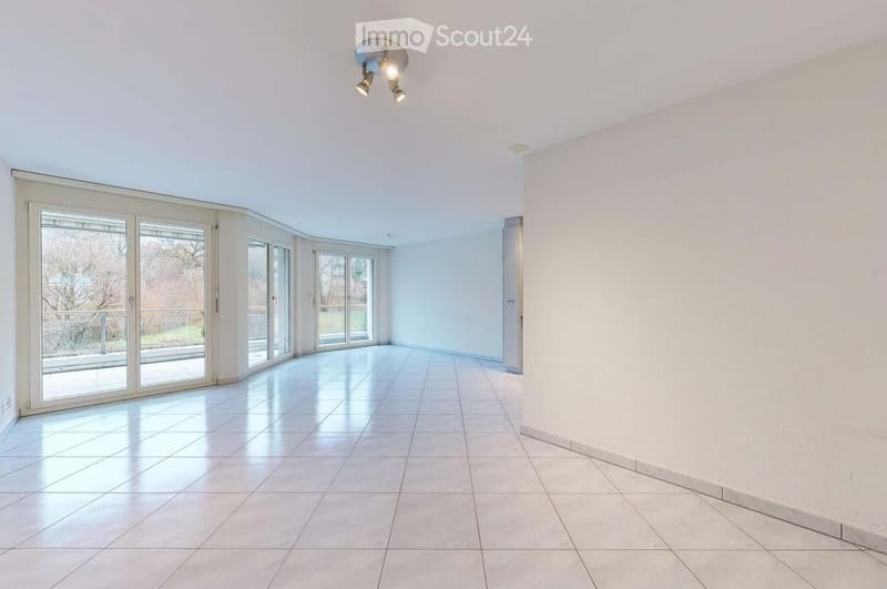 Empty room with white walls, tiled floor, large sliding glass doors leading to an outdoor area, and recessed ceiling lighting.