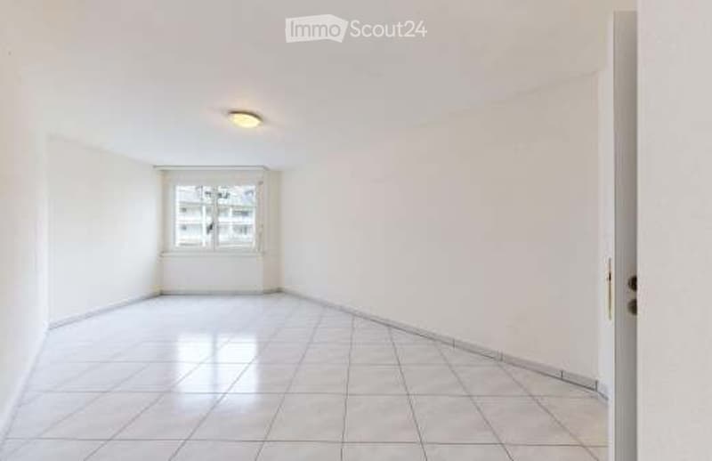 Completely empty room with white tiled floor, white walls, a single window, and a ceiling light fixture.