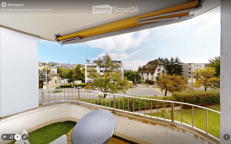 Balcony with a view of the city, featuring a round table and a chair, metal railing, and a retractable awning.