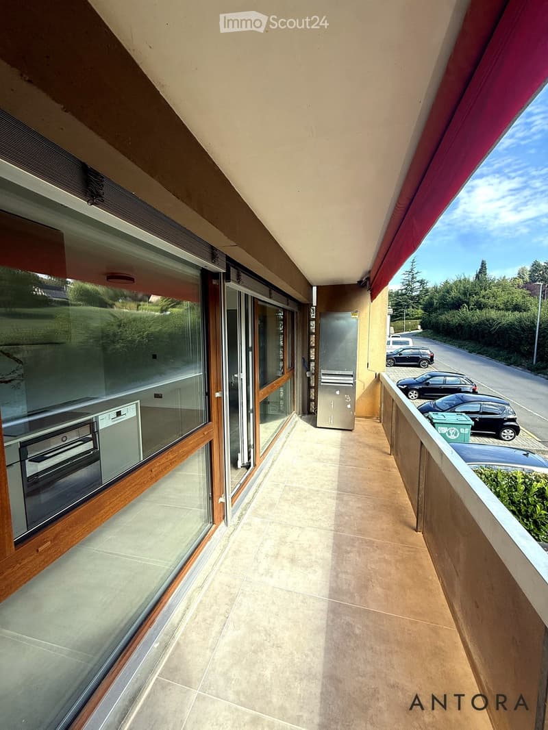 Balcony with tiled floor, glass sliding doors, view of street and parked cars, mailbox, and greenery.