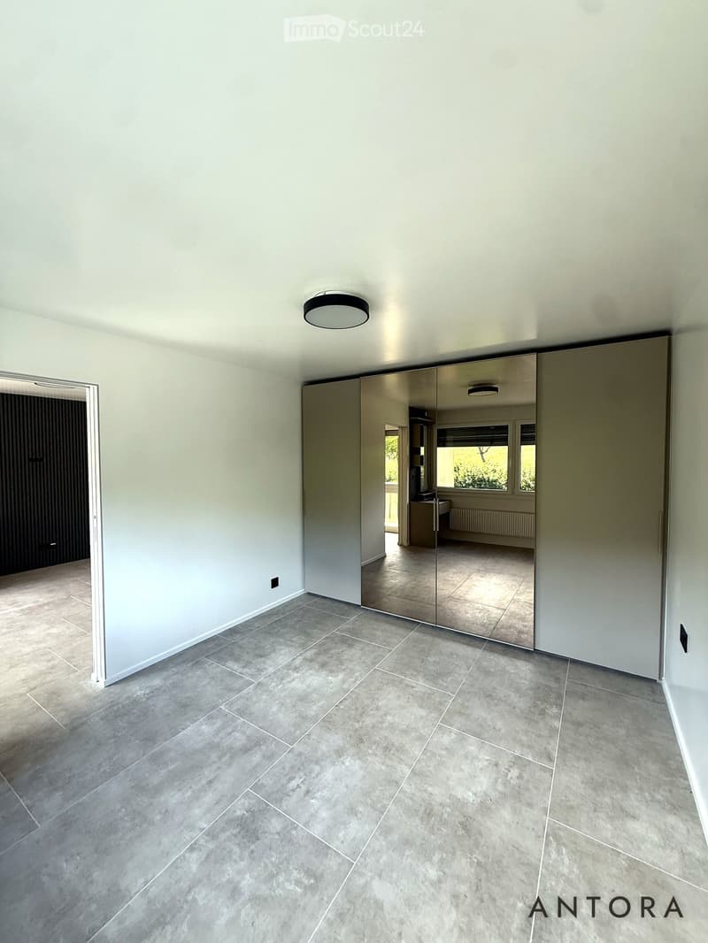 Empty room with light grey tiled flooring, white walls, and a large mirrored sliding door leading to another space.