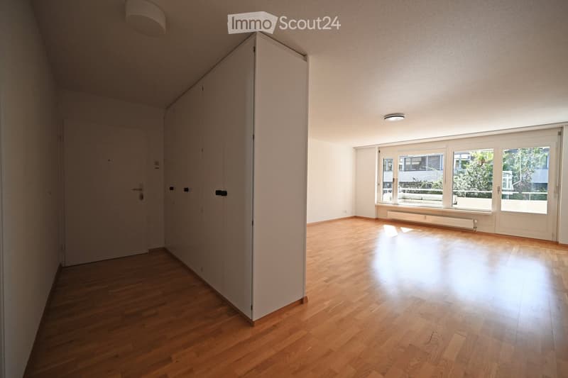 Empty room with wooden flooring, white walls, large windows, and a door leading to another space.