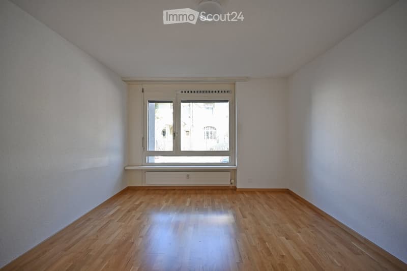 Empty room with wooden flooring, white walls, and a large window with double panes. The room has a simple, clean design with no furniture or decorations.