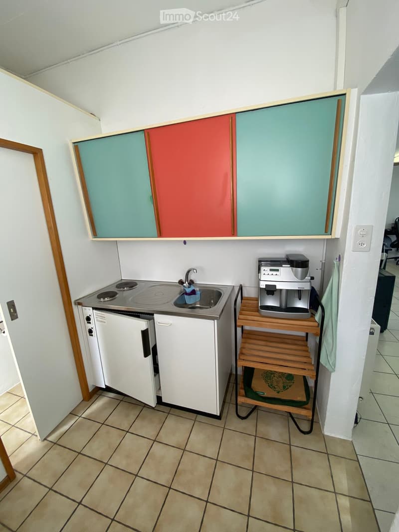 Compact kitchen with a sink, faucet, coffee maker on a wooden stand, and white cabinets with colorful doors.