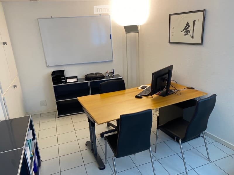 A modern office space with a wooden table, chairs, a computer setup, a whiteboard, and a framed picture on the wall.