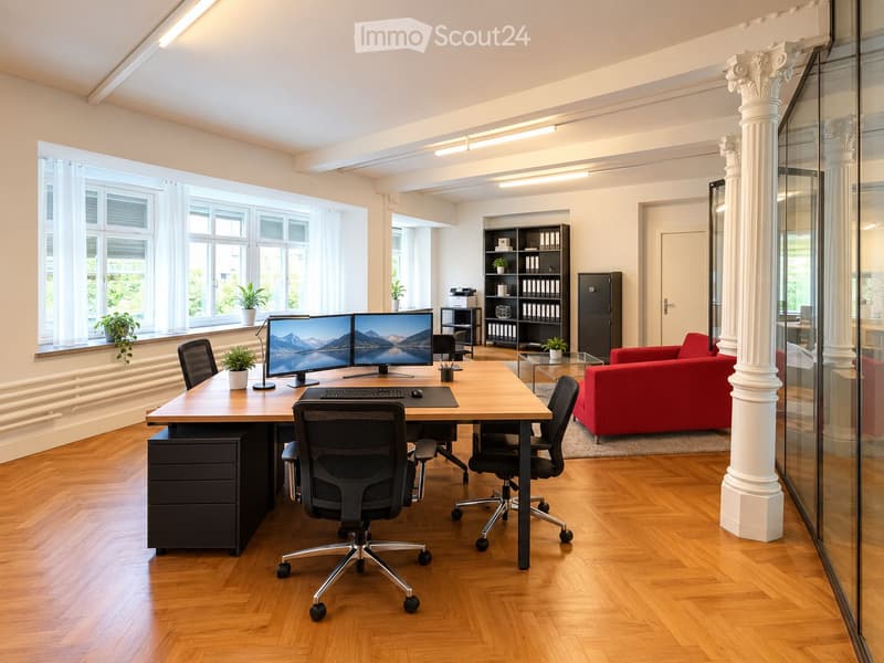 A modern, well-lit office space with a large wooden desk, multiple computer screens, ergonomic chairs, a red sofa, and a bookshelf with books and decorative items.