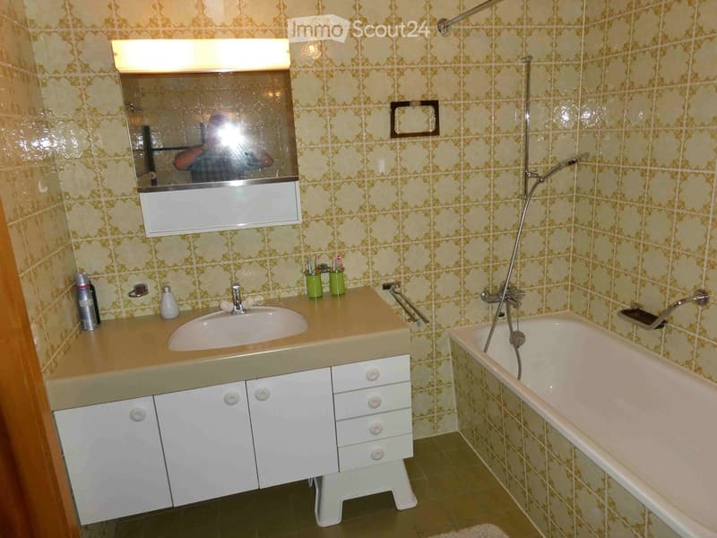 Bathroom with a sink, bathtub, mirror, and cabinet. The walls are tiled with a floral pattern, and the floor is tiled in a dark green color.