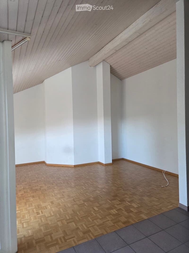 Empty room with wooden herringbone flooring, white walls, and white ceiling beams. No furniture or equipment present.