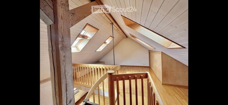 An attic space with wooden beams, exposed wooden ceiling, skylights, and a wooden staircase leading to a lower level.
