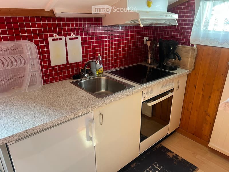 Modern kitchen with red tiled backsplash, granite countertop, stainless steel sink, electric stove, and white cabinets.