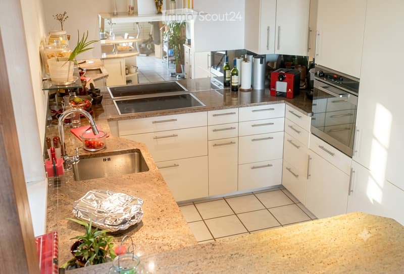 Modern kitchen with white cabinets, stainless steel appliances, granite countertops, and a sink with a modern faucet. The space includes an induction cooktop, oven, coffee maker, and various kitchen items on the counter.