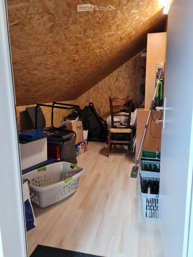 Cozy attic space with wooden walls and slanted ceilings, featuring a wooden chair, laundry basket, storage bins, and cleaning supplies.