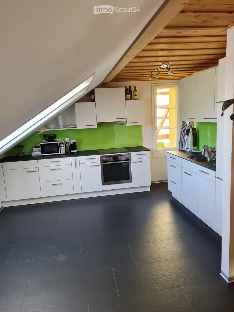 Modern kitchen with white cabinets, dark countertops, and a green backsplash. Features an oven, microwave, coffee maker, and a window with a view.