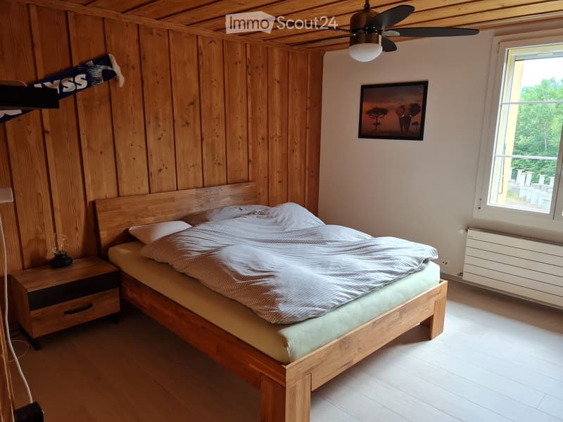 Cozy bedroom with wooden walls and ceiling, featuring a wooden bed with striped bedding, a nightstand with a lamp, and a framed picture on the wall.