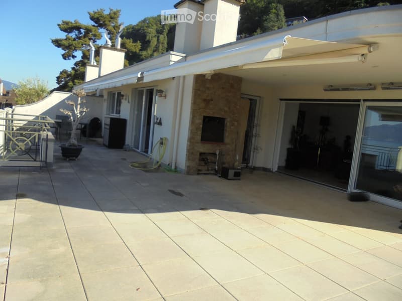 Spacious outdoor patio with tiled flooring, covered area with retractable awning, sliding glass doors leading to the house, small tree in a pot, and a gated area with a bicycle.